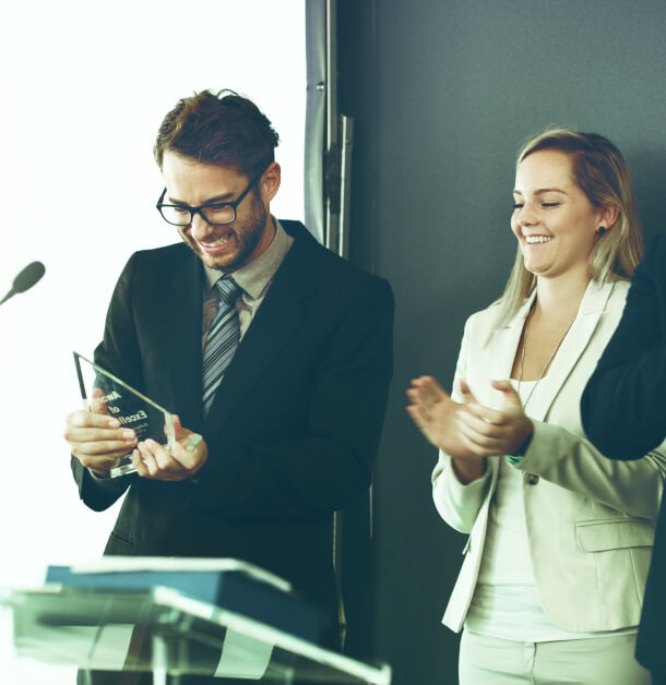 A suited man receives an award for excellence in analytics, while a woman applauds, celebrating Austin PR success in crisis management.