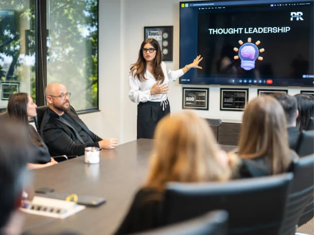 A woman presents a "Thought Leadership" slide on SEO and Public Relations to colleagues in an Austin PR consulting conference room.