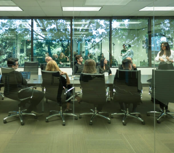 A group in a glass-walled meeting room in Austin discusses Public Relations strategies, Crisis Management, and Social Media consulting.