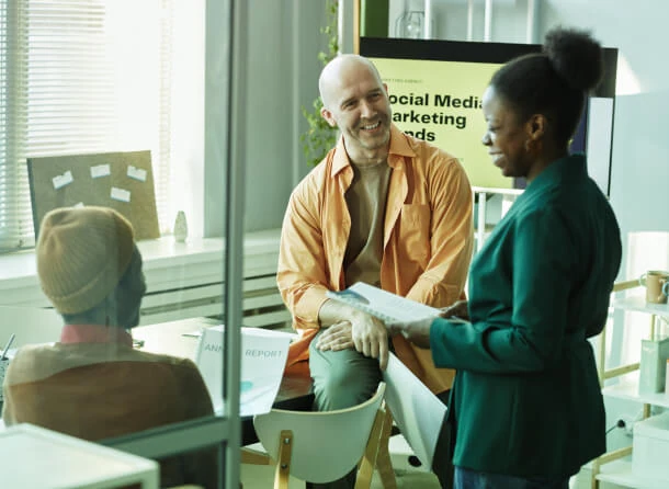 Three people in an Austin PR firm discuss social media strategies, focusing on thought leadership and crisis management with a "Social Media Marketing Trends" board in the background.